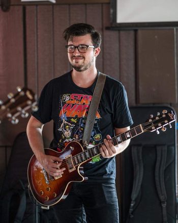 A man with glasses, wearing a Star Wars t-shirt, playing an electric guitar.